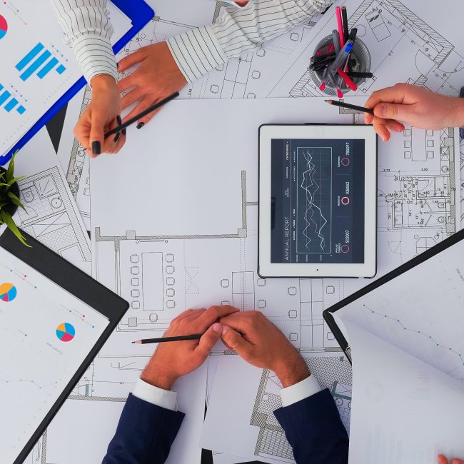 Ein Foto von oben auf ein Schreibtisch mit Zeichnungen und Händen, die ein Projekt managen.